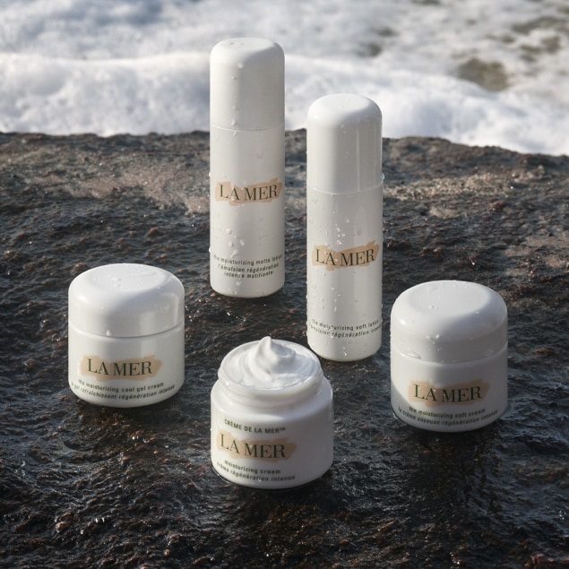 Group of moisturiser and lotion container and bottles sitting on a rock ledge near the ocean.